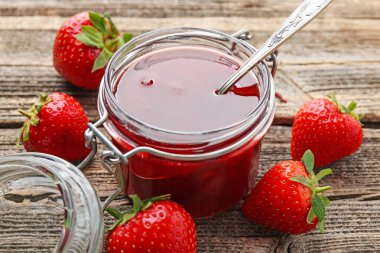 Cam kavanozda lezzetli çilek reçeli ve ahşap masada taze böğürtlen, yakın plan.