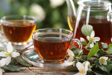 Lezzetli yasemin çayı fincanda, çaydanlık ve çiçekler ahşap masada, yakın plan.