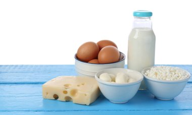 Farklı süt ürünleri ve yumurtalar mavi ahşap masada beyaz arka planda