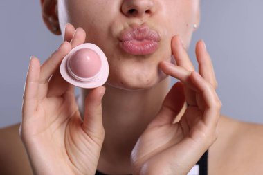 Açık gri arka planda dudak merhemi olan genç bir kadın, yakın plan.