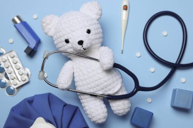 Pediatri konsepti. Steteskoplu oyuncak ayı, termometre ve açık mavi arka planda haplar, düz uzanma