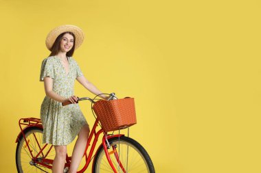 Şapkalı gülümseyen kadın, açık yeşil arka planda sepeti olan bisikletli poz veriyor. Metin için boşluk