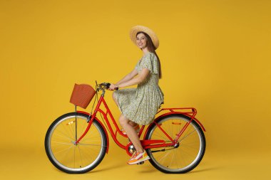 Sarı arka planda sepeti olan şapkalı gülümseyen bir kadın.