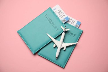Biletli pasaportlar ve pembe arka planda uçak modeli, üst manzara.