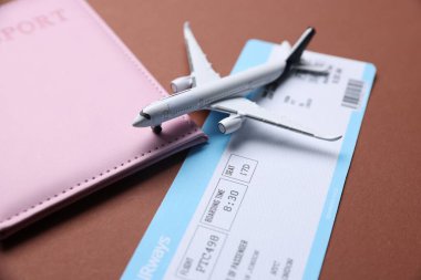 Uçak modeli, uçuş bileti ve kahverengi arka planda pasaport, yakın plan.