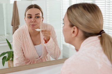Kadın evin içinde aynanın yanında yüzüne krem sürüyor. Sivilce tedavisi
