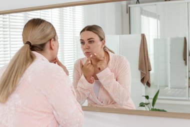 Banyoda aynanın yanında sivilce çıkaran bir kadın. Sivilce sorunu