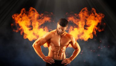 Arkasında yanan kanatları olan esmer bir vücut geliştirici. Gömleksiz, kaslı adam duman içinde.