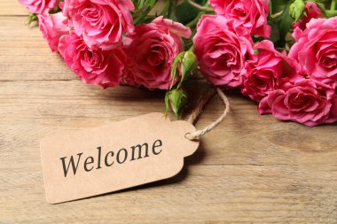 Hoş geldin kartı ve gül buketi ahşap masada, yakın plan