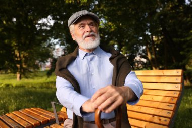 Dışarıda bankta oturan bastonlu yakışıklı yaşlı adam.