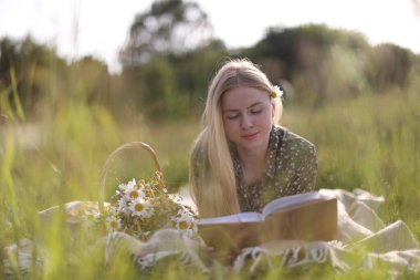 Bir buket kır çiçeğiyle çayırda kitap okuyan güzel bir kadın.