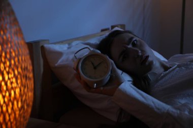 Evde yatağında uykusuzluk çeken, çalar saati olan hayal kırıklığına uğramış bir kadın.