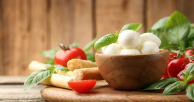 Lezzetli mozzarella peyniri topları, domatesler, fesleğen ve grissini ahşap masada, yakın plan. Kamera sağa hareket ediyor