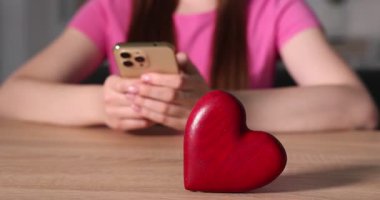 Online flört sitesi. Ahşap masada akıllı telefon kullanan kadın dekoratif kalbe odaklan.