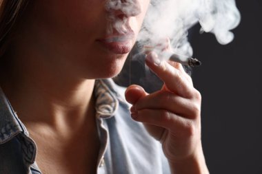 Arka planda sigara içen tişörtlü bir kadın, yakın plan. Kötü alışkanlık.