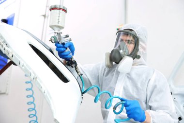 Kaportacıda sprey boyayla araba boyuyor.