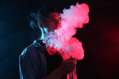 Koyu arkaplandaki neon ışıklarda elektronik sigara içen adam