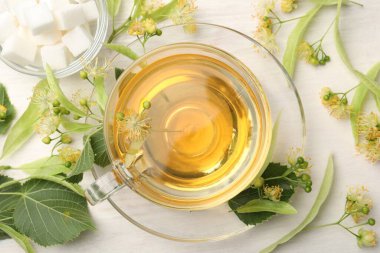 Fincanda taze ıhlamur çayı, küp şekerler ve beyaz ahşap masa üzerinde çiçekler, düz uzanmış