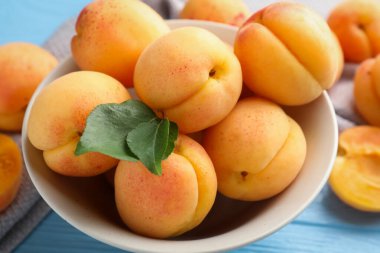 Açık mavi ahşap masada yeşil yapraklı taze kayısılar, yakın plan.