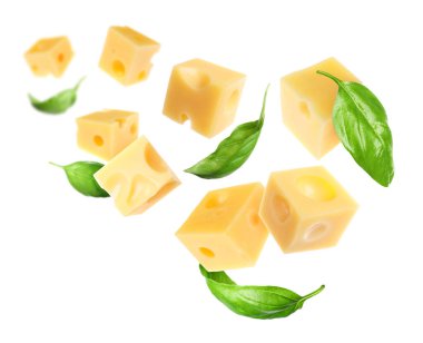 Peynir küpleri ve yeşil fesleğen yaprakları beyaz arka planda uçuşuyor