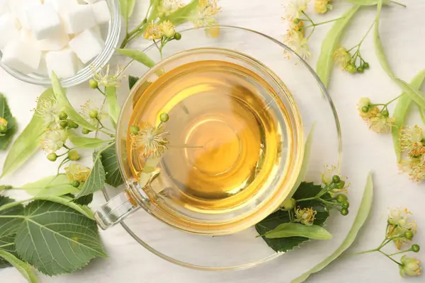 Fincanda taze ıhlamur çayı, küp şekerler ve beyaz ahşap masa üzerinde çiçekler, düz uzanmış