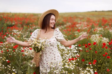 Gülümseyen kadın elinde papatya çiçekleri ile yaban çiçeği çayırında doğanın tadını çıkarıyor.