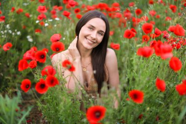 Kırmızılı gelincik çiçekleri arasında gülümseyen kadının portresi.