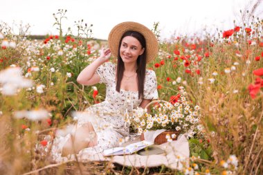 Yaban çiçeği çayırında poz veren şapkalı gülümseyen kadın.