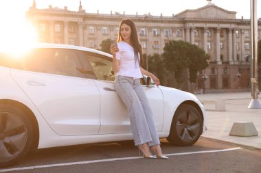 Güneşli bir günde modern arabanın yanında akıllı telefonu olan güzel bir kadın.