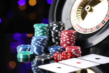 Kumarhane fişleri, iskambil kartları, rulet tekerleği ve zarlar ayna yüzeyinde bulanık ışıklara karşı, yakın plan