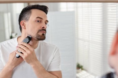 Evde aynanın yanında tıraş makinesiyle tıraş olan yakışıklı bir adam. Metin için boşluk