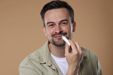 Yakışıklı bir adam açık kahverengi arka planda dudaklarına merhem sürüyor.