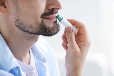 Bulanık ışık arka planında dudaklarına dudak kremi süren bir adam.