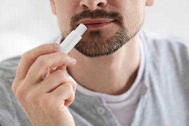 Bulanık ışık arka planında dudaklarına dudak kremi süren bir adam.