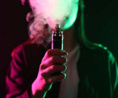 Siyah arka planda neon lambalarda elektronik sigara içen kadın, yakın plan