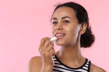 Gülümseyen kadın pembe arka planda dudaklarına merhem sürüyor.