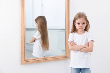 Evdeki aynanın yanındaki üzgün küçük kız.