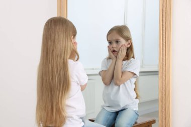 Üzgün küçük kız aynada kendine bakıyor.