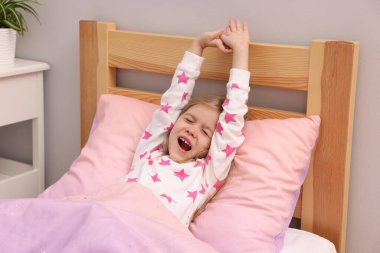 Küçük kız evde yatakta uyanıyor.