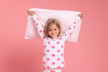 Pembe arka planda yastıklı pijamalı şirin bir kız.