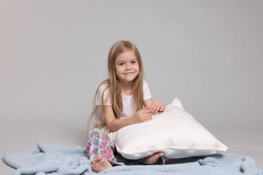 Pijamalı, gri arka planda yastıklı, sevimli küçük bir kız.
