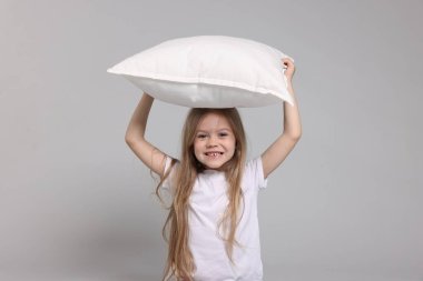 Gri arka planda yastıklı pijamalı şirin bir kız.