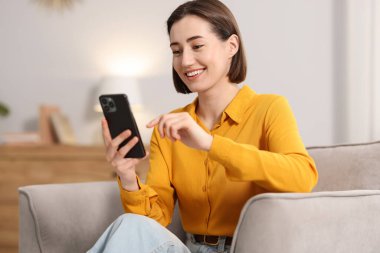 Evdeki koltukta modern akıllı telefon kullanan bir kadın.