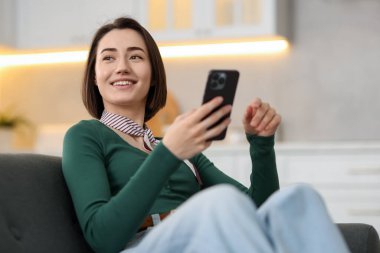 Evdeki koltukta modern akıllı telefon kullanan bir kadın.