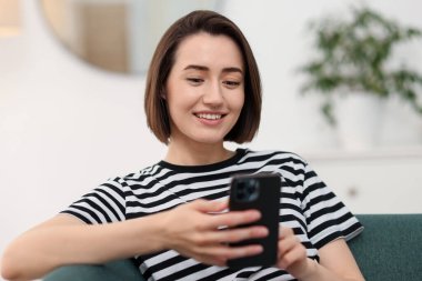 Evdeki koltukta modern akıllı telefon kullanan bir kadın.