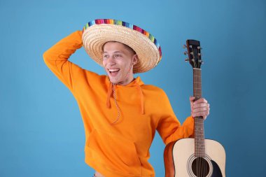 Açık mavi arka planda gitarı olan şapkalı mutlu adam.