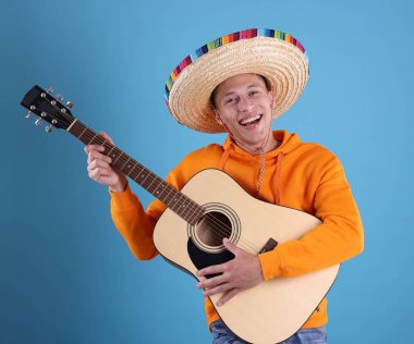 Şapkalı mutlu adam açık mavi arka planda gitar çalıyor.
