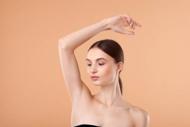 Bej arka plandaki epilasyondan sonra pürüzsüz bir ten gösteren genç kadın.