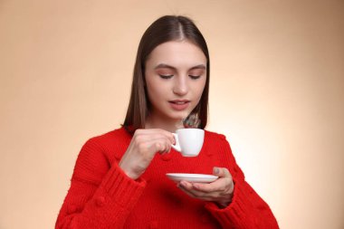 Bej renkli arka planda fincandan kahve içen kadın