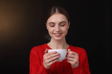 Kahverengi arka planda bir fincan kahveyle gülümseyen kadın.